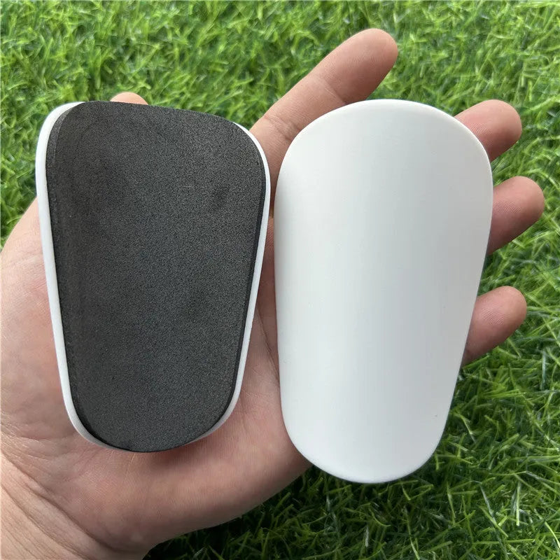 Extra small black and white plastic football shin guards for junior players, shown at 8x5 cm size.