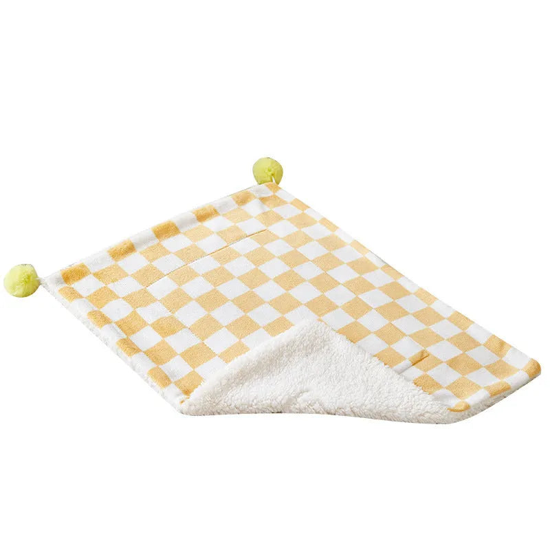 Green plaid pet fleece blanket with fur ball decoration on a sofa for a cat or dog.