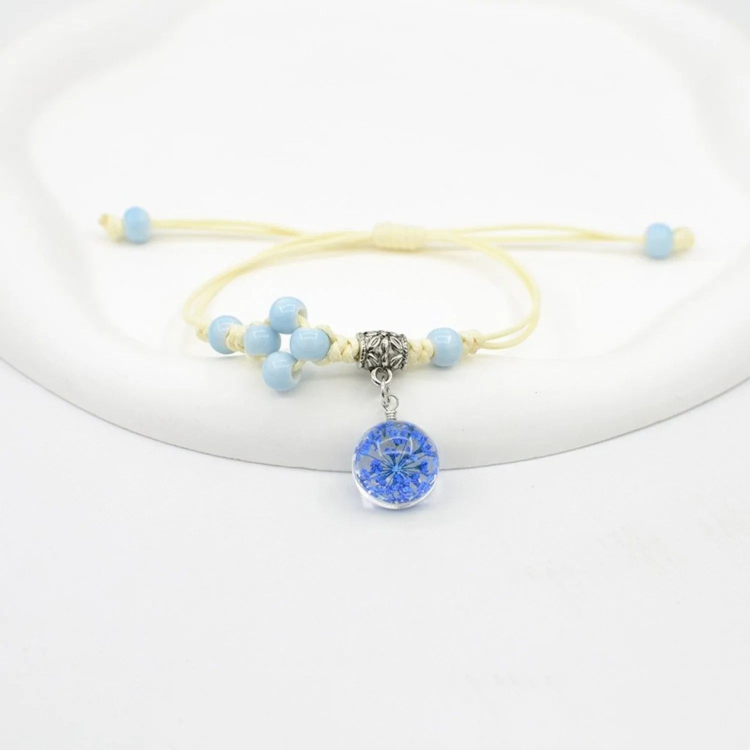 Close-up of a hand-woven glass bracelet with large beads containing real dried flowers and a lace design.