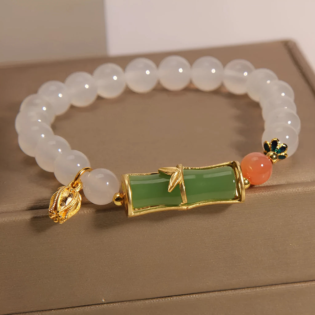 Close-up of a women's bracelet with a white agate jade bead and bamboo joint design on a natural background.