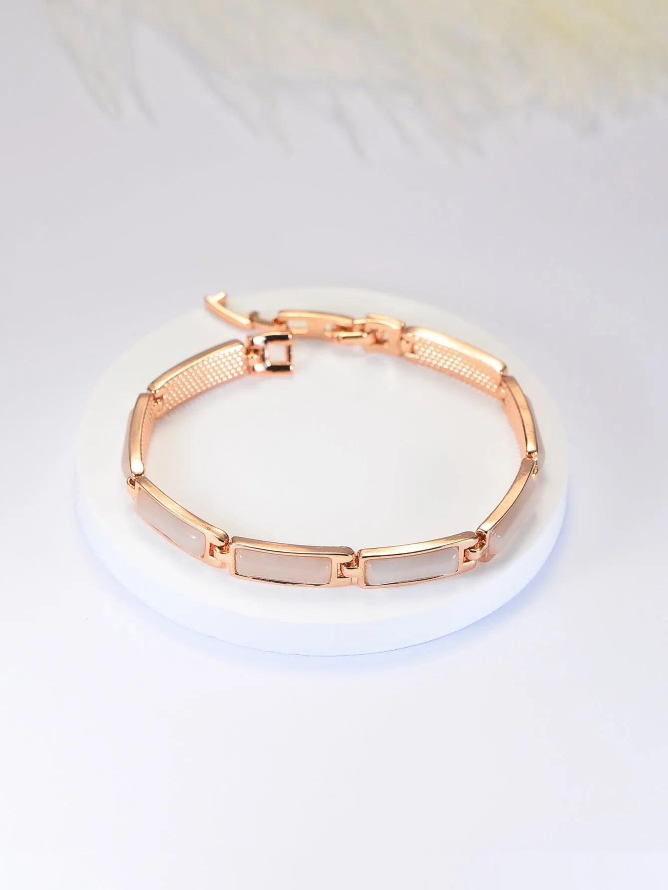 Women's geometric rose gold opal bracelet with quadrilateral shape and gemstone inlay on a plain background