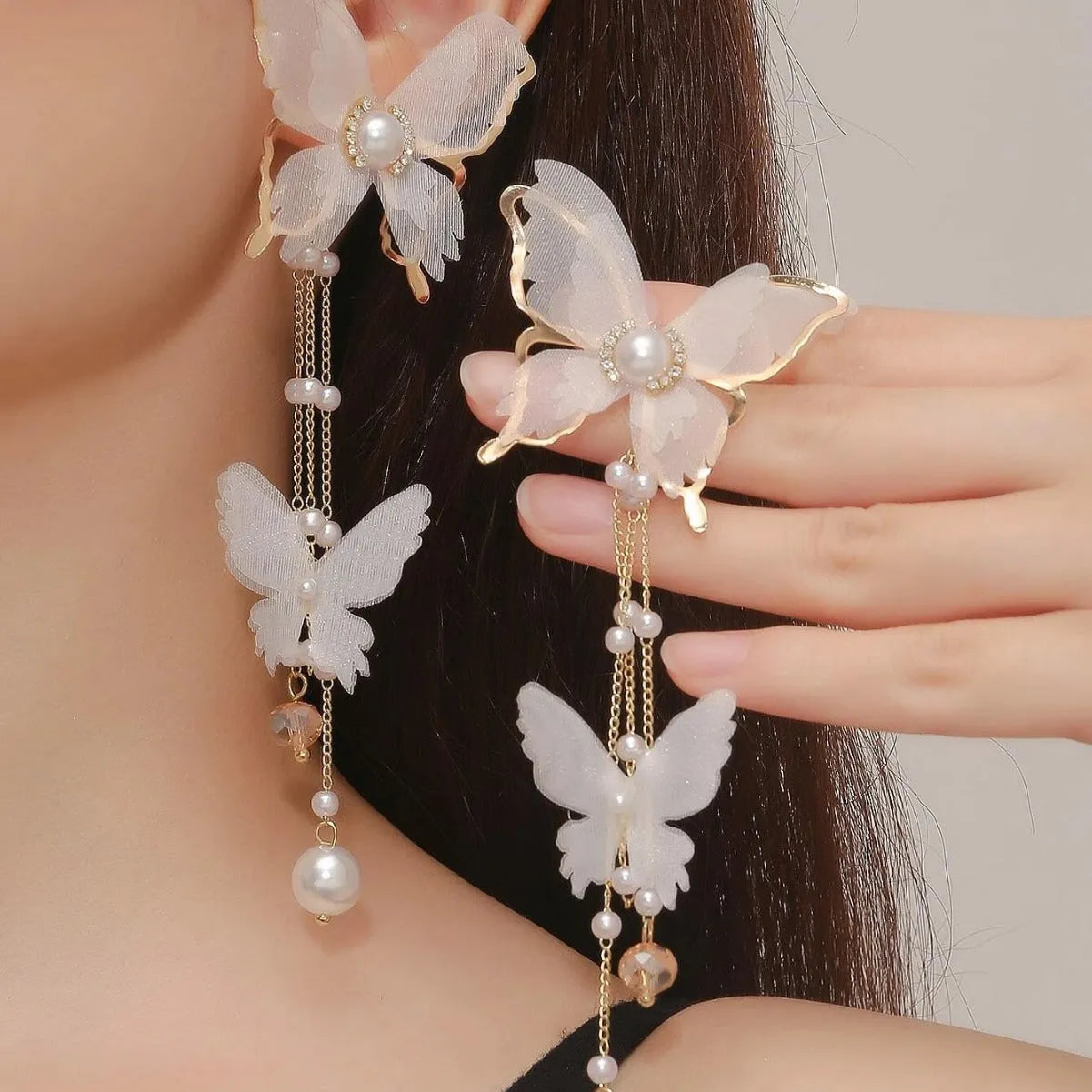 A pair of white butterfly-shaped earrings with pearls, rhinestones, and a dangling lace tassel.