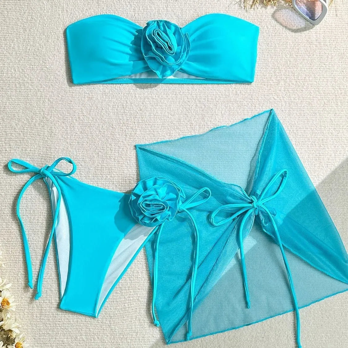 Blue women's tube top swimsuit with a large 3D tied flower, matching pants, and a skirt laid flat.