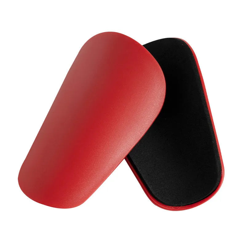 Two pairs of PU mini shin guards in black, white, red, and dream blue colours on a sports field.