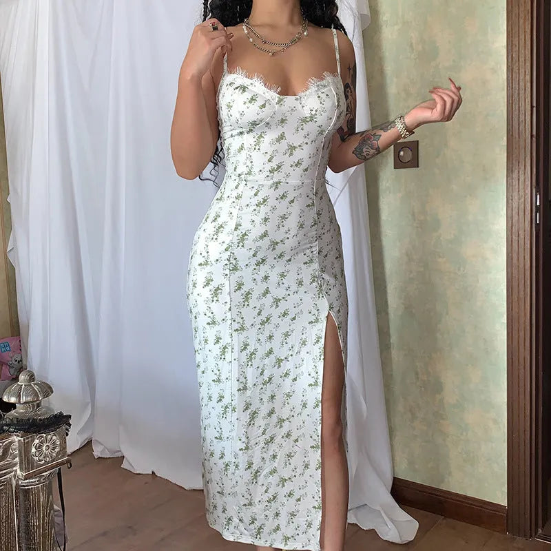 A woman wearing a long blue dress with a lace floral print, a side slit and thin suspender straps.