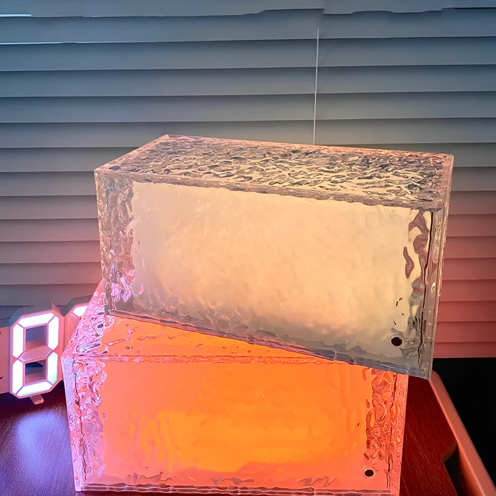 Clear acrylic geometric ice cube shaped night lamp glowing with multi-coloured LED light on a dark surface.