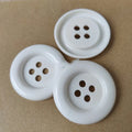 Assortment of oversized round plastic buttons in multiple colours with four stitching holes.