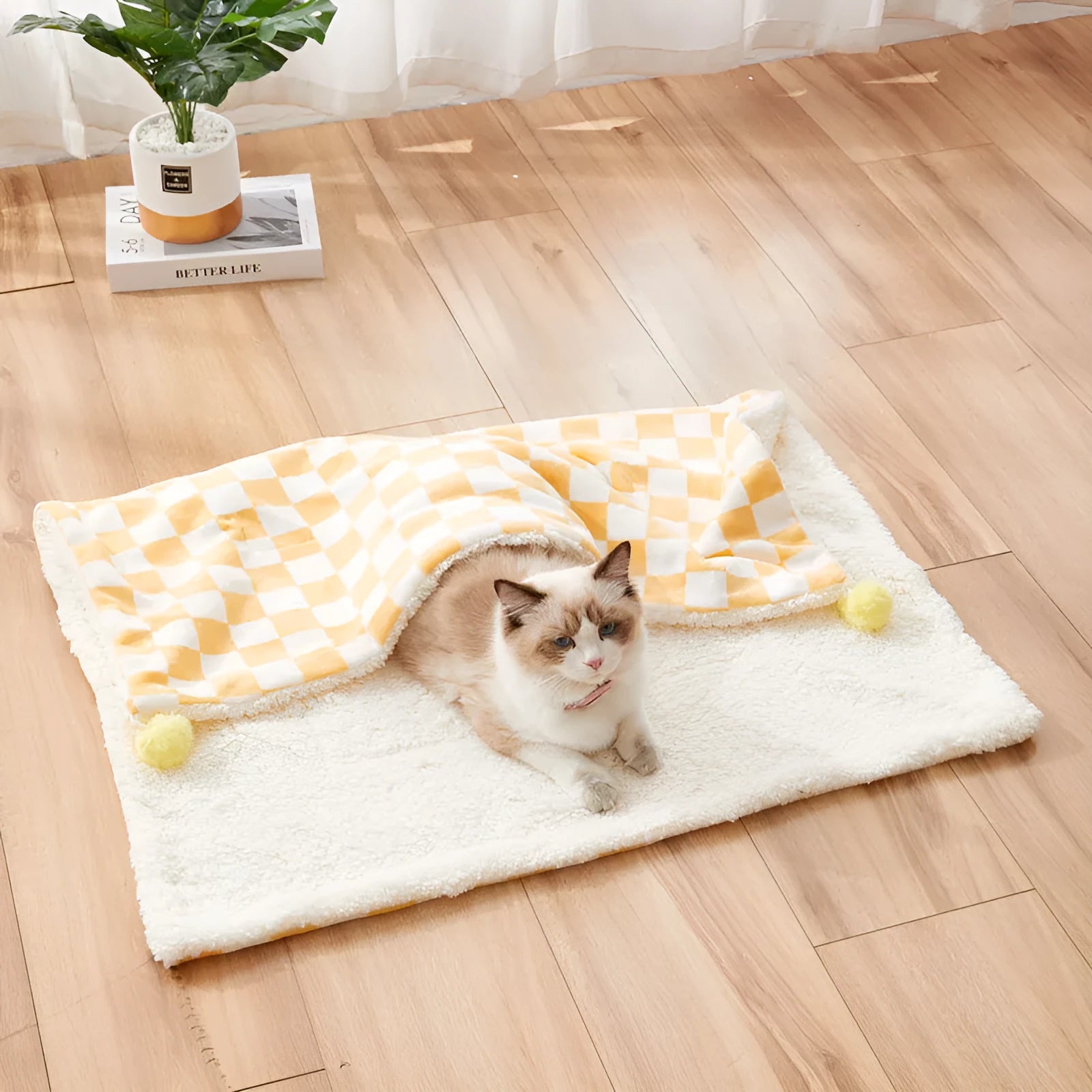 Green plaid pet fleece blanket with fur ball decoration on a sofa for a cat or dog.