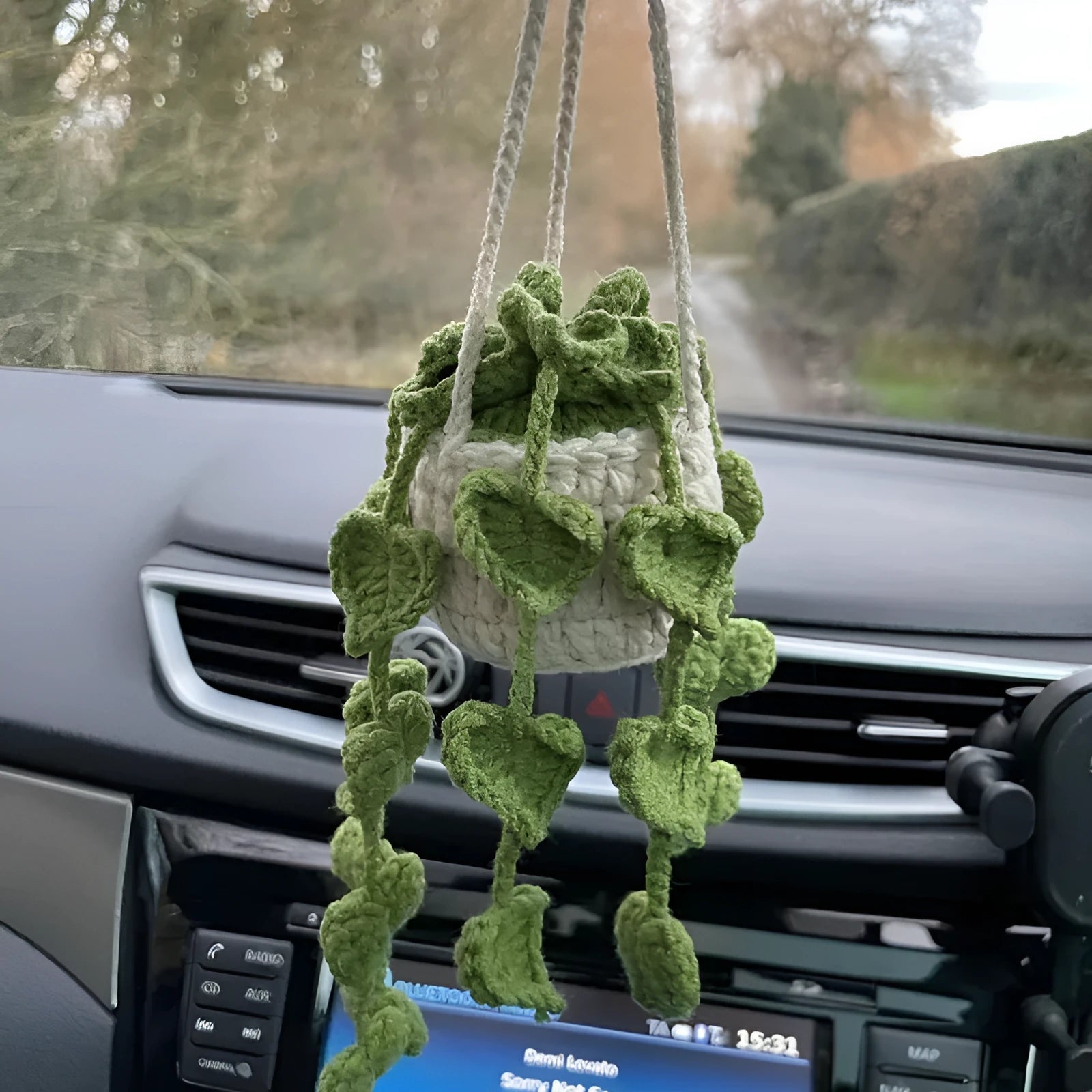 Green and white knitted wool car plant decoration with hanging rope on a car dashboard.