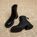 Women's black ankle boot with flat heel and back zipper on a plain background.