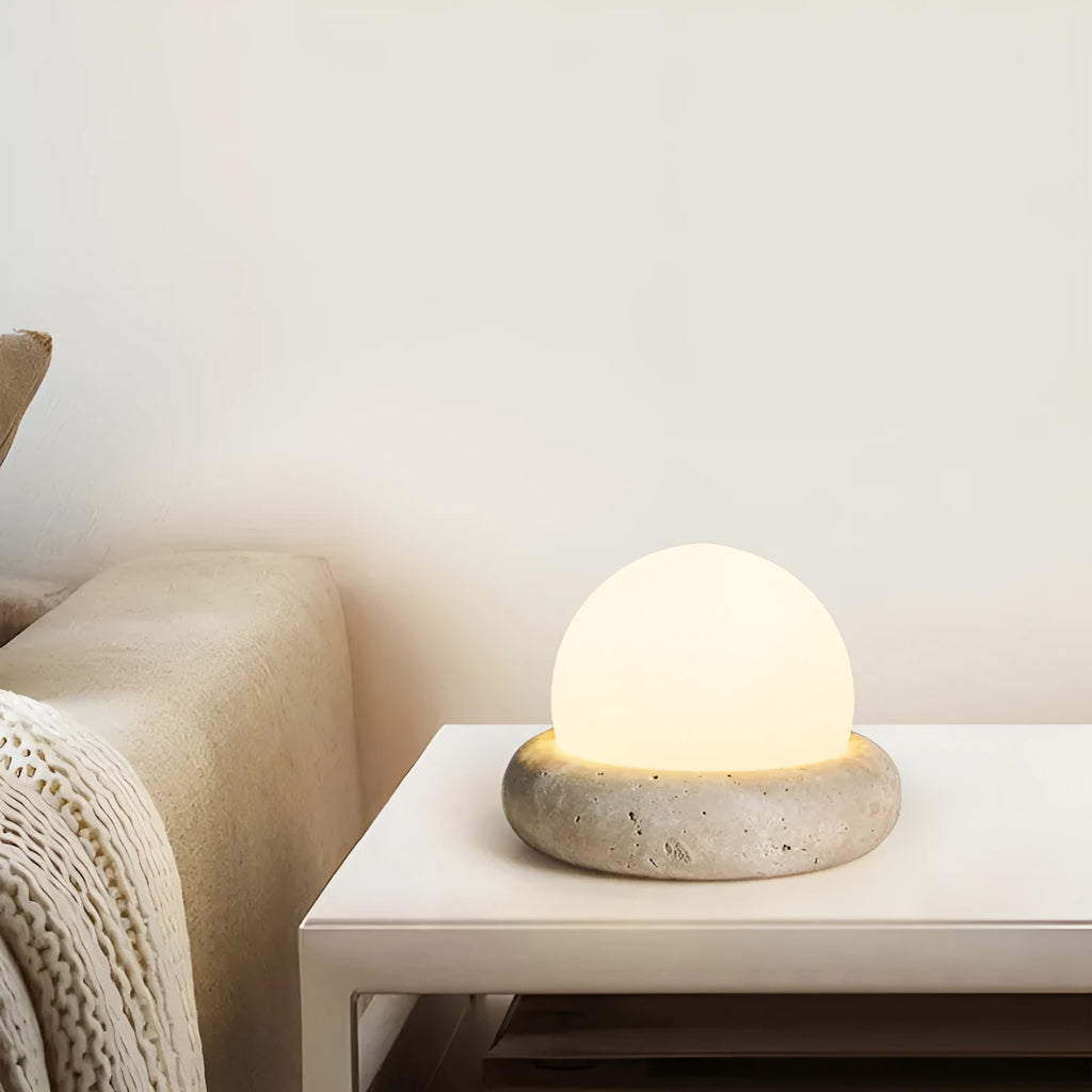 Cream coloured round rechargeable remote control night light on a bedside table.