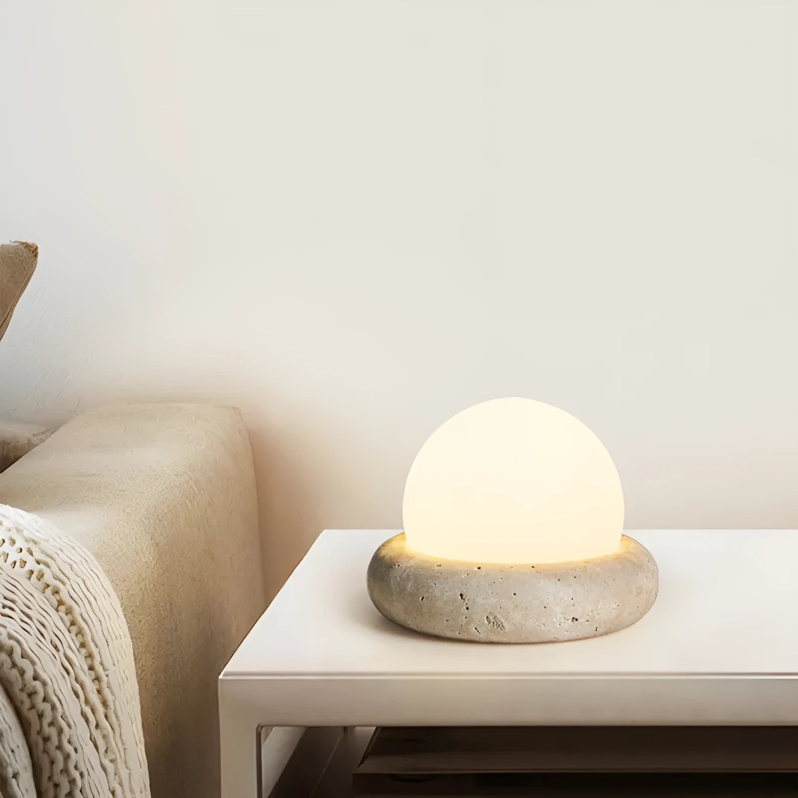 Cream coloured round rechargeable remote control night light on a bedside table.