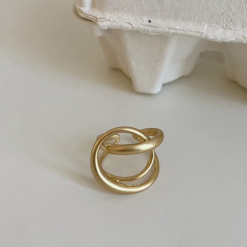 Geometric open ring with 3D interlaced matte metal design in gold or silver finish.