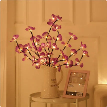 Pink artificial Phalaenopsis orchid branch LED decorative light, 65cm tall, on a bedside table.