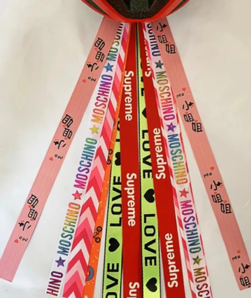 Colourful fabric helmet streamers for children's roller skating and ski helmets, shown in apricot, red, and grey.