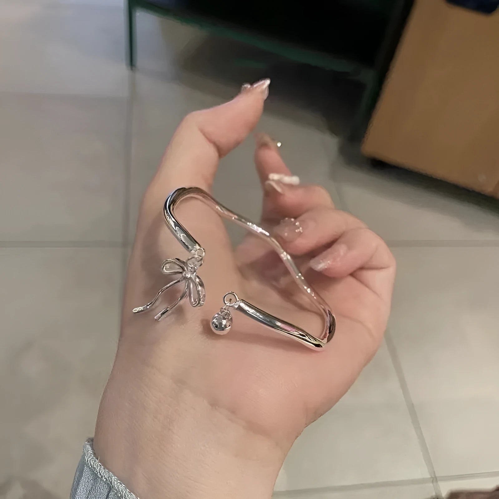 Silver bow charm adjustable bracelet with electroplated finish and bell opening mechanism