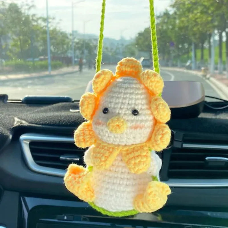 Green and white knitted wool car plant decoration with hanging rope on a car dashboard.