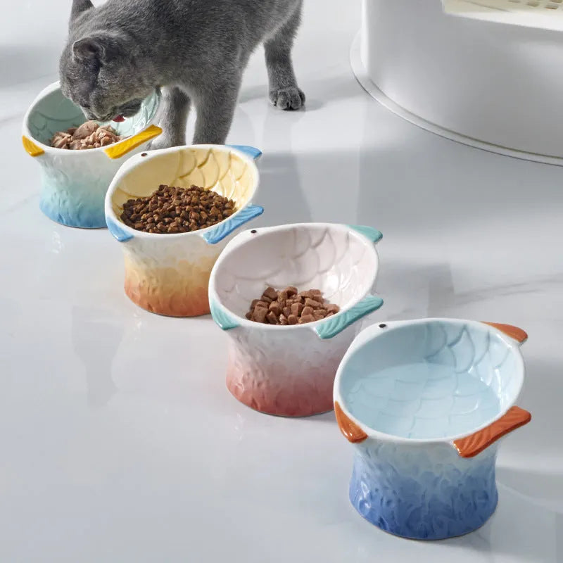 Blue fish-shaped ceramic cat feeder bowl with shallow tilt angle and non-slip base on a wooden surface.