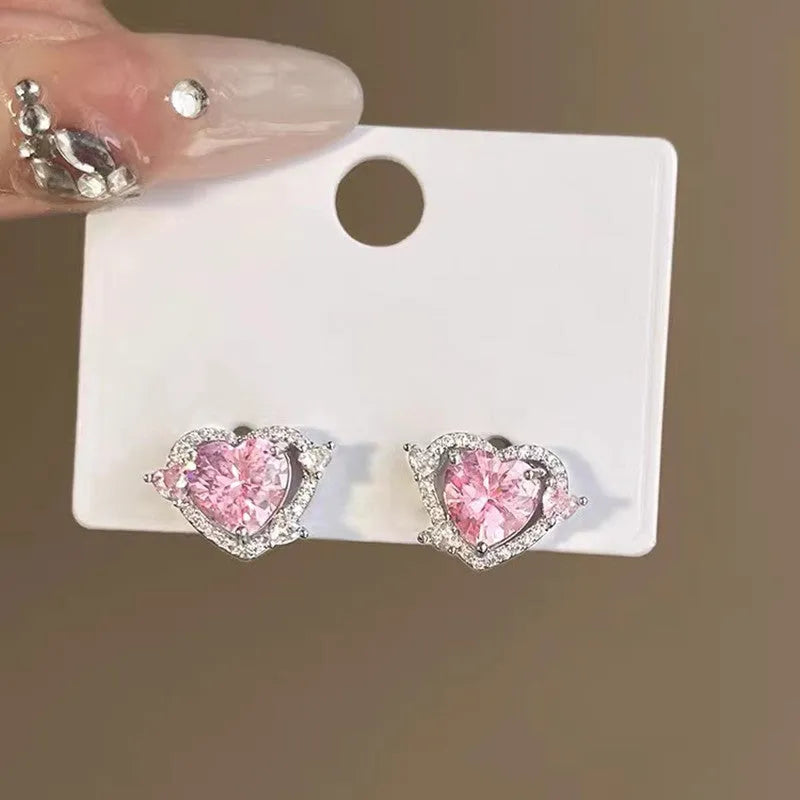A pair of small white gold coloured heart shaped stud earrings for women on a jewellery card.