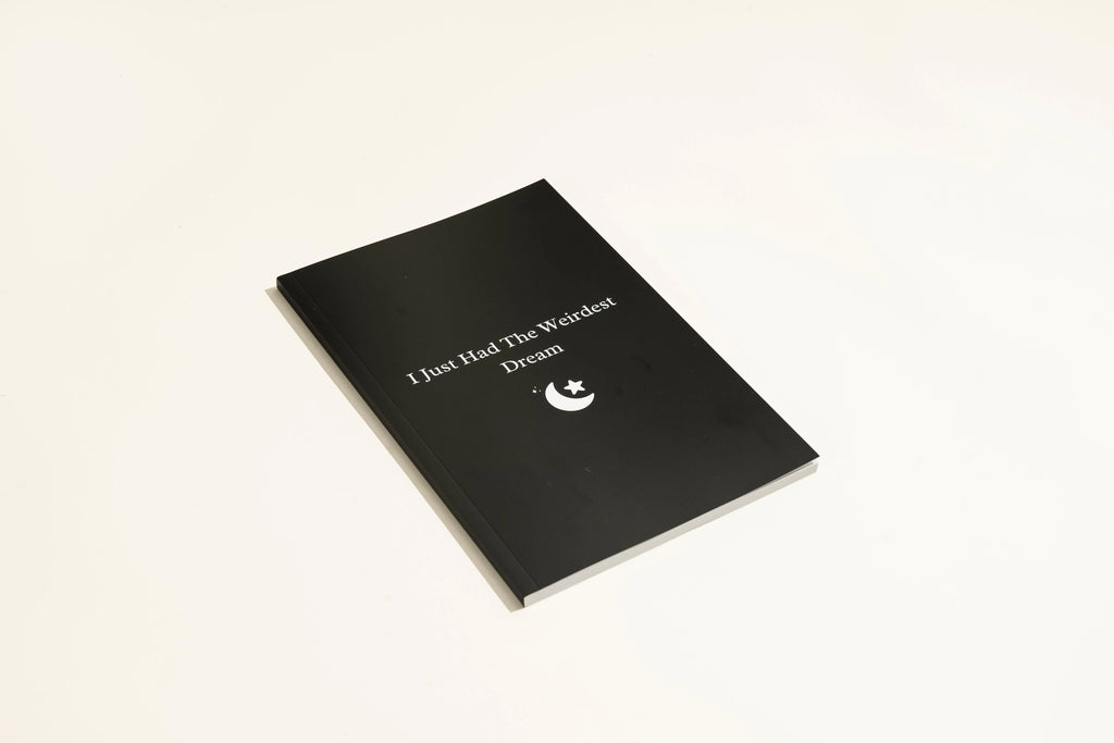 Black covered dream journal notebook open to show cream dot grid pages