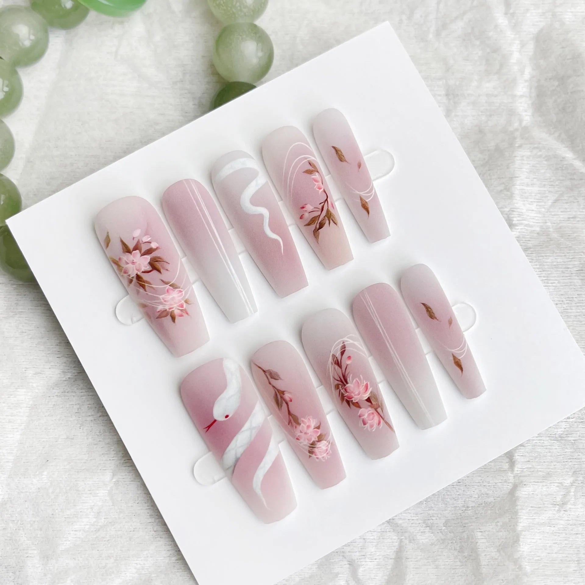 Ancient Chinese style snake year red prefabricated nail tips in drunk flower colour, long ladder shape, on a display stand