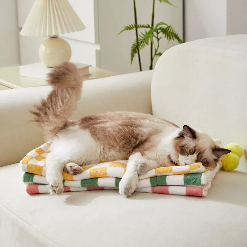 Green plaid pet fleece blanket with fur ball decoration on a sofa for a cat or dog.