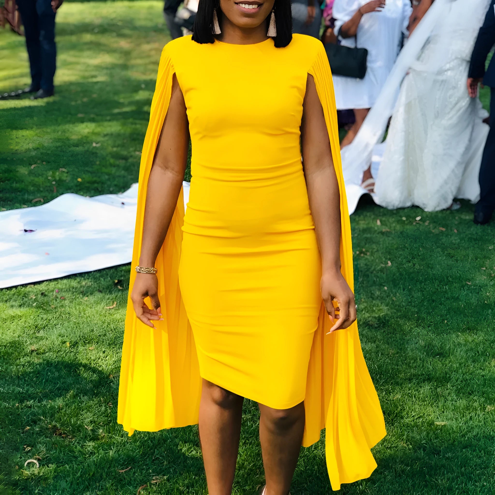A model wearing a yellow high-waist evening gown with long sleeves and a pleated floor-length skirt.