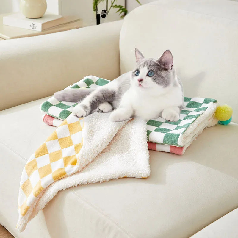 Green plaid pet fleece blanket with fur ball decoration on a sofa for a cat or dog.