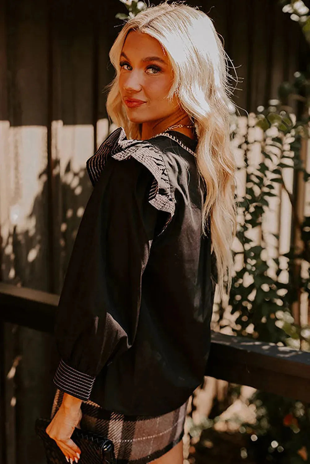 Black women's long sleeve blouse with V-neck, contrast stitching, and ruffle sleeve details.