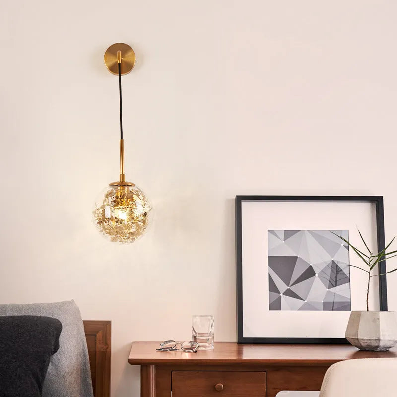 Simple modern glass wall lamp in golden flower finish mounted beside a bed.