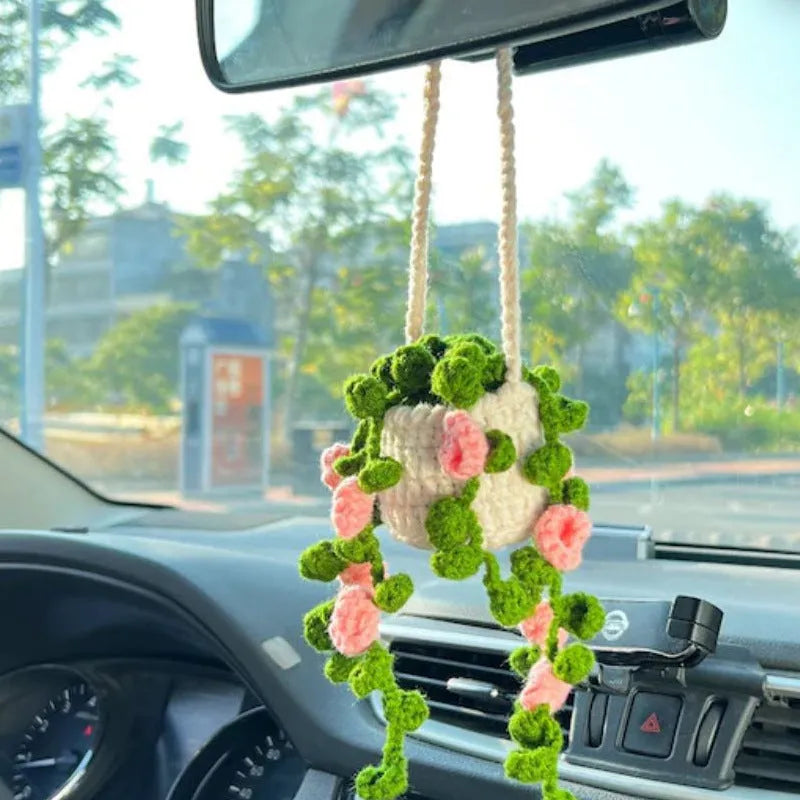 Green and white knitted wool car plant decoration with hanging rope on a car dashboard.