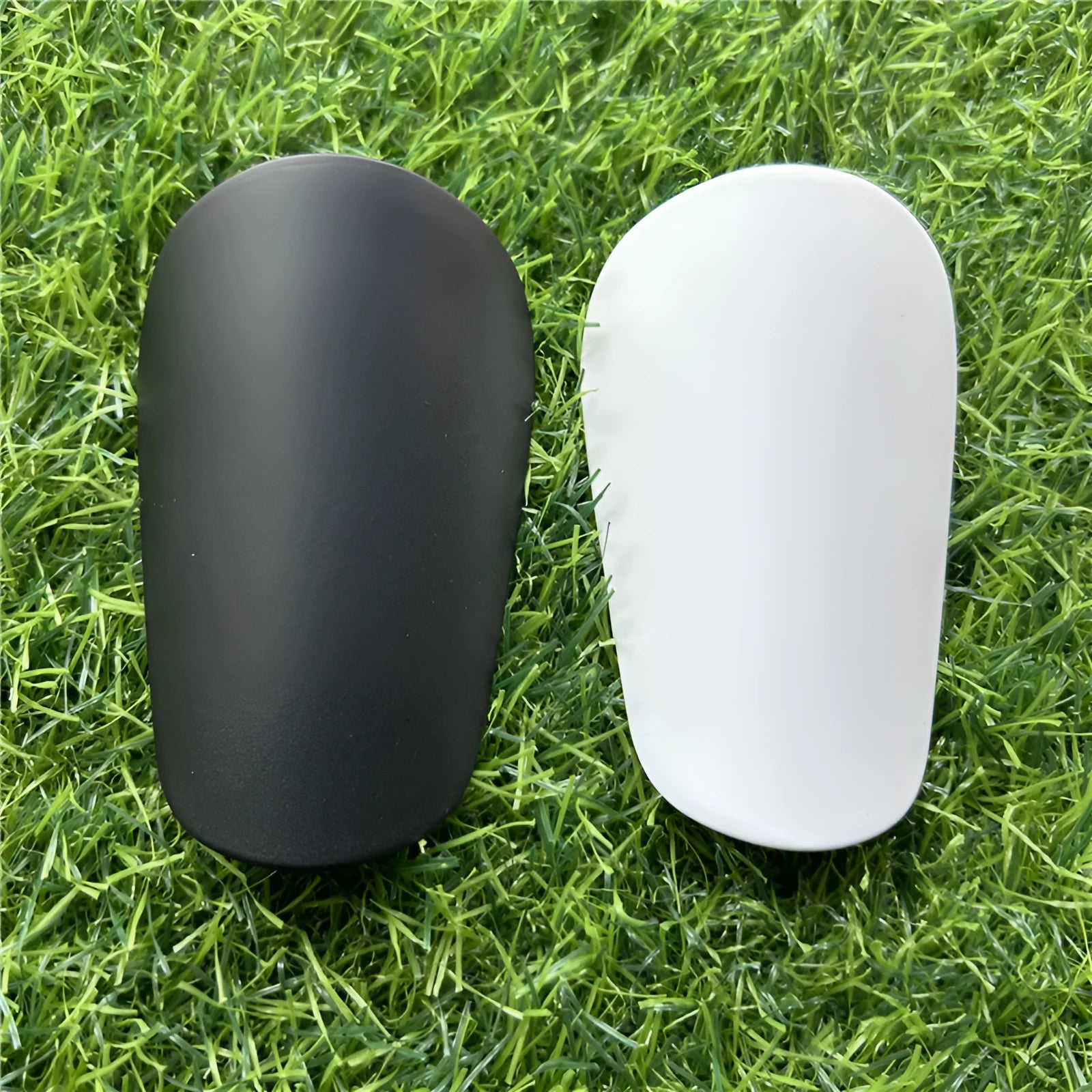 Extra small black and white plastic football shin guards for junior players, shown at 8x5 cm size.
