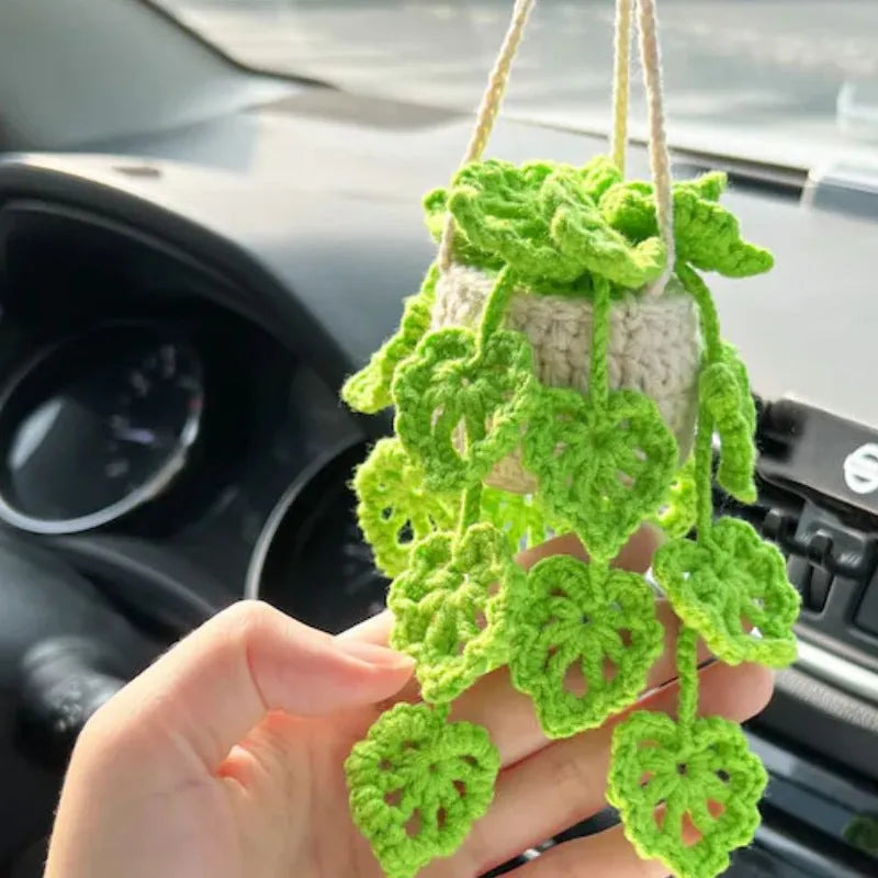 Green and white knitted wool car plant decoration with hanging rope on a car dashboard.