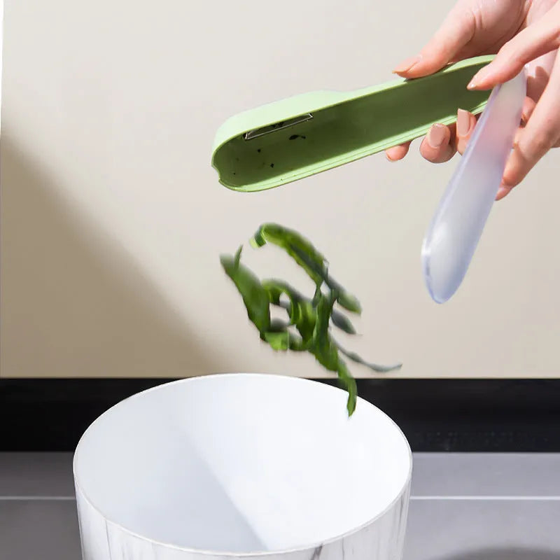 Dark green vegetable peeler with a storage tube and a stainless steel blade on a kitchen worktop.