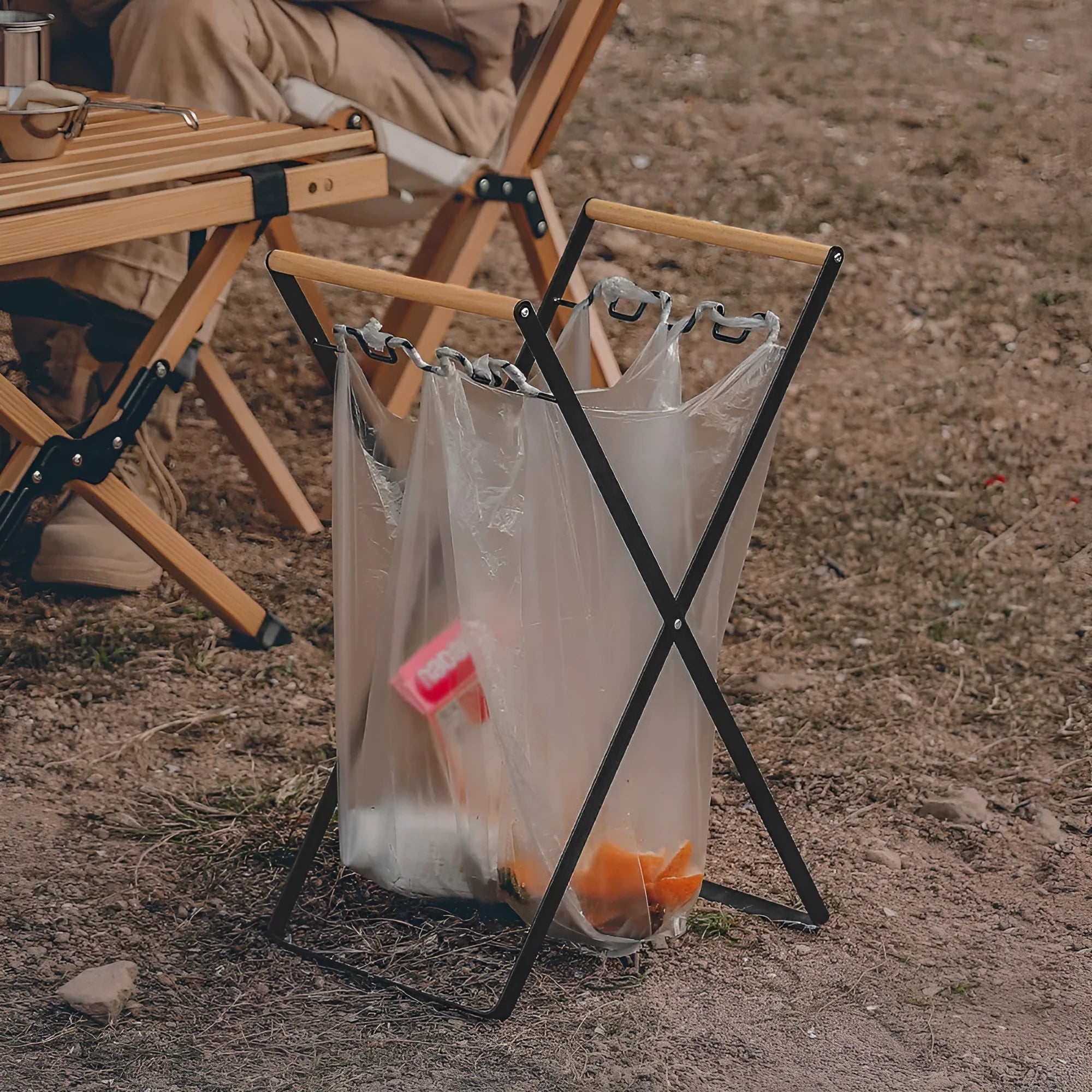 Black outdoor folding iron trash rack with a wooden handle, holding a bin bag.