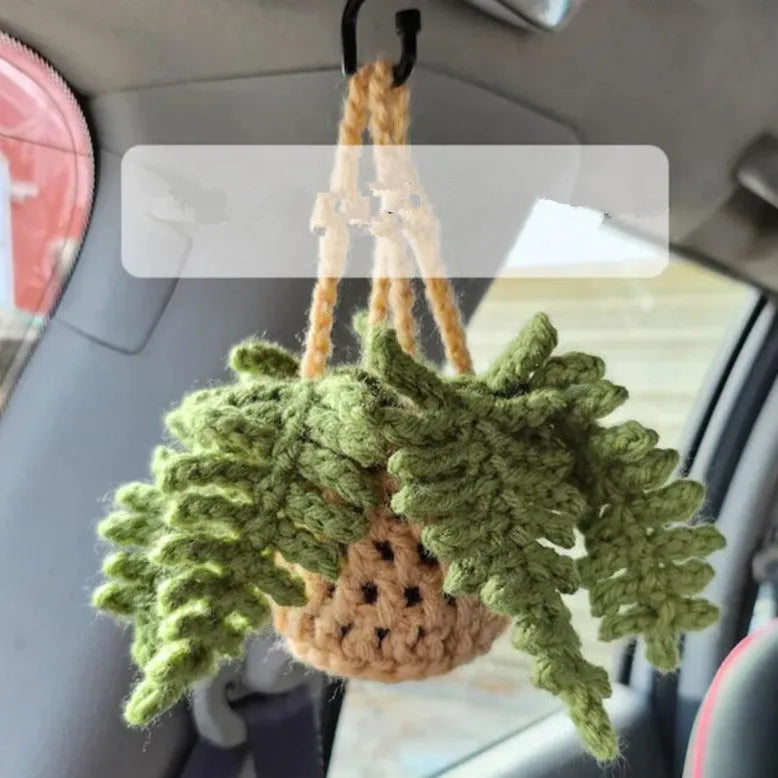 Green and white knitted wool car plant decoration with hanging rope on a car dashboard.
