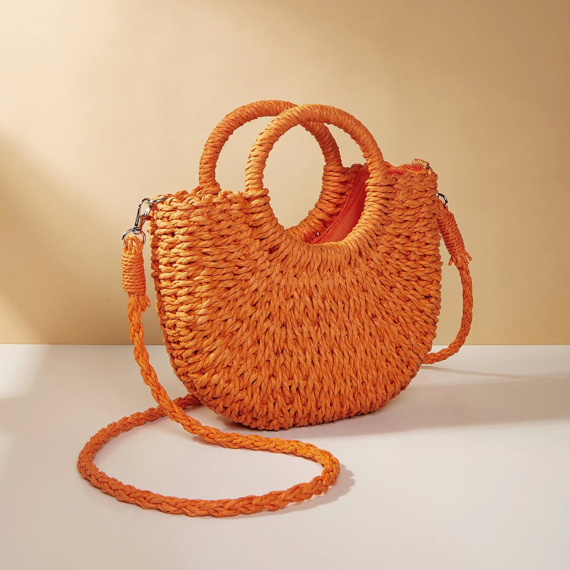 Woven straw beach bag in beige, peach skin lining, crossbody style, 24cm height, on a sandy beach