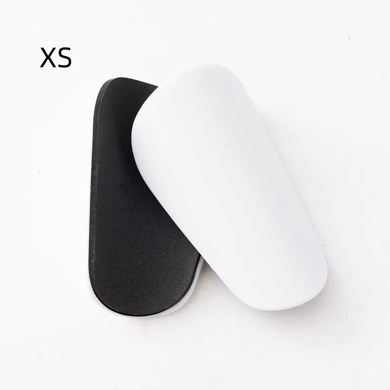 Two pairs of PU mini shin guards in black, white, red, and dream blue colours on a sports field.