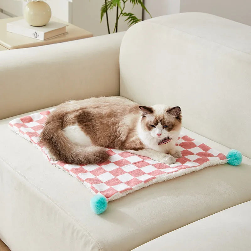 Green plaid pet fleece blanket with fur ball decoration on a sofa for a cat or dog.