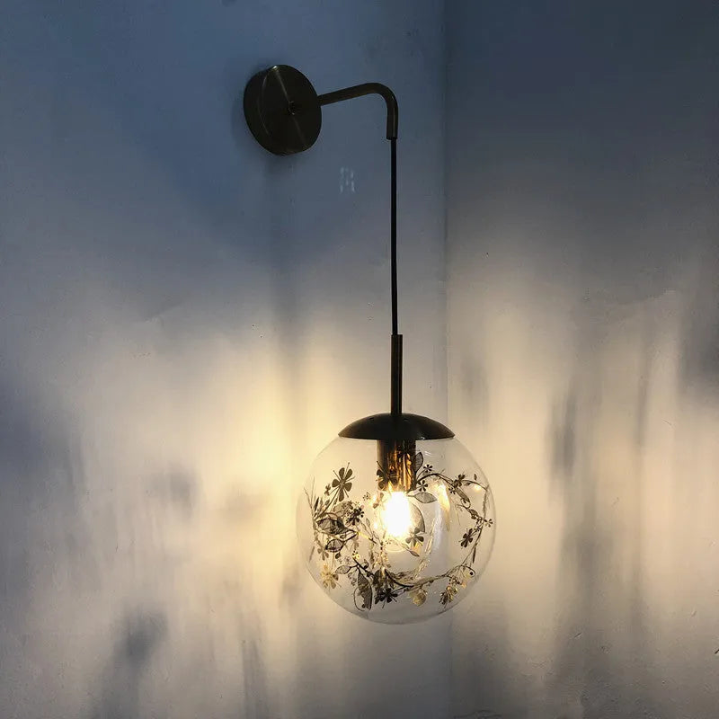 Simple modern glass wall lamp in golden flower finish mounted beside a bed.