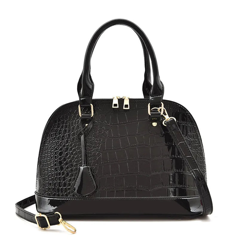 Large shiny black crossbody shoulder bag with a structured shell shape.
