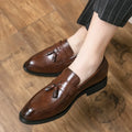 Men's black tassel loafers with a slip-on design and rubber sole on a plain background.
