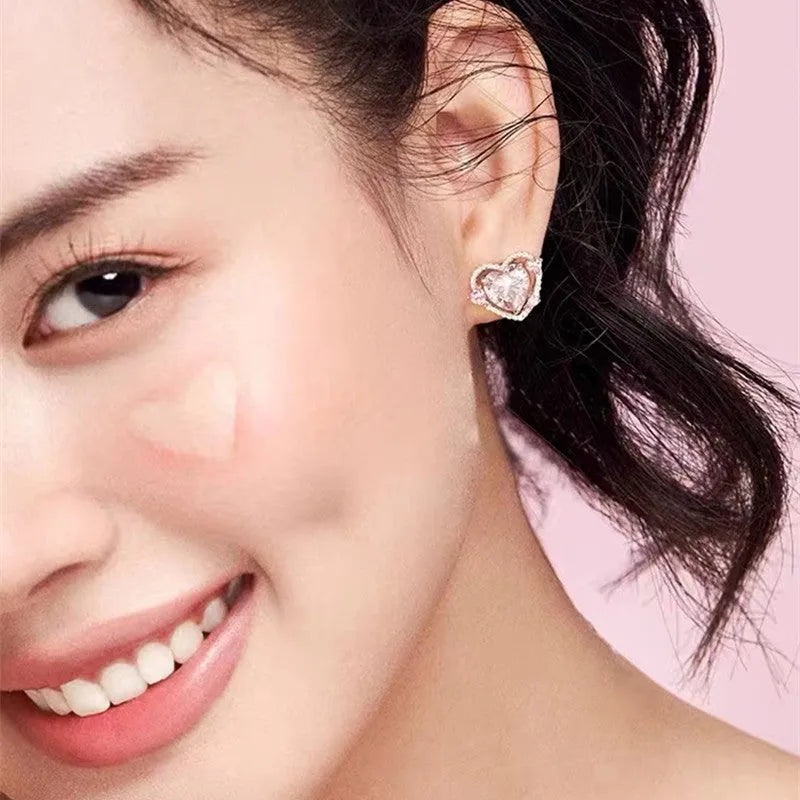 A pair of small white gold coloured heart shaped stud earrings for women on a jewellery card.