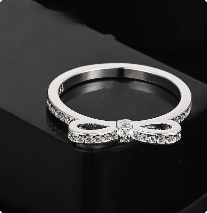 Silver bow-shaped ring with rhinestone and zircon crystal details on a model finger.