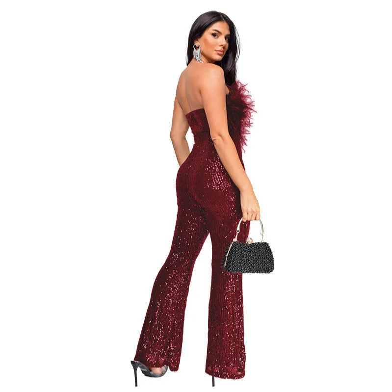 A woman wearing a black sleeveless, backless jumpsuit with sequin and feather details on the torso and flared legs.