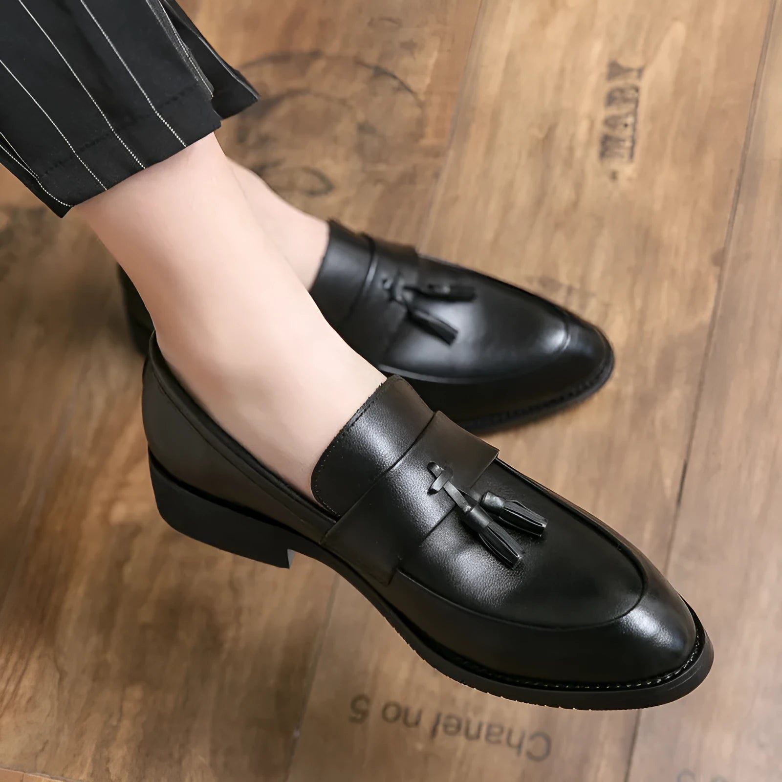 Men's black tassel loafers with a slip-on design and rubber sole on a plain background.