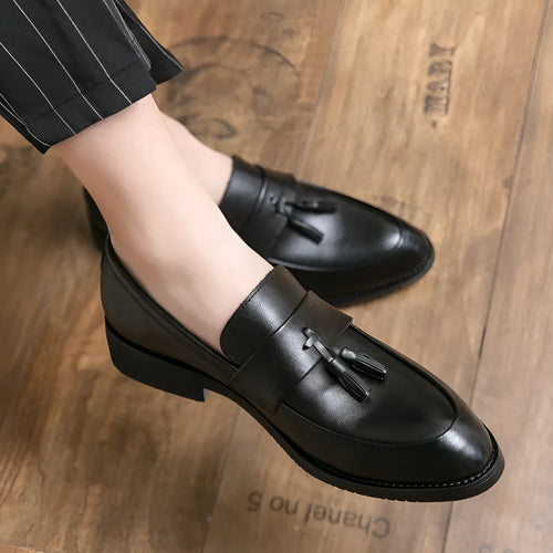 Men's black tassel loafers with a slip-on design and rubber sole on a plain background.