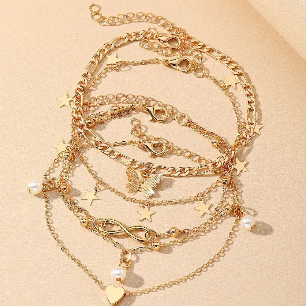Four gold-tone alloy anklets with butterfly and heart pearl charms arranged as a set