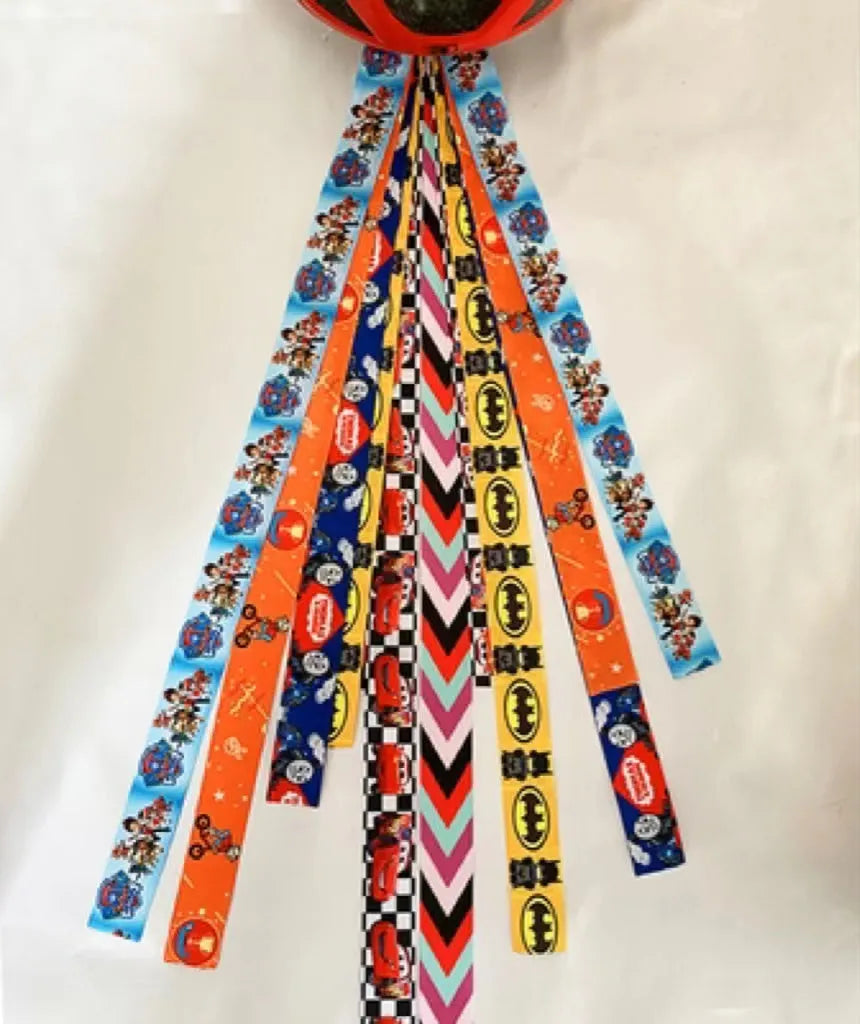 Colourful fabric helmet streamers for children's roller skating and ski helmets, shown in apricot, red, and grey.