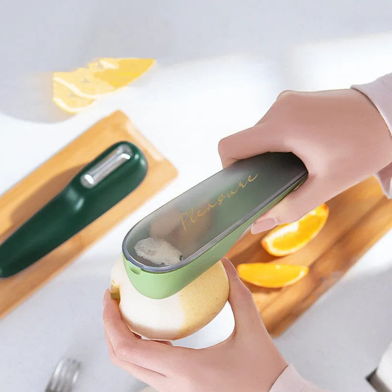 Dark green vegetable peeler with a storage tube and a stainless steel blade on a kitchen worktop.